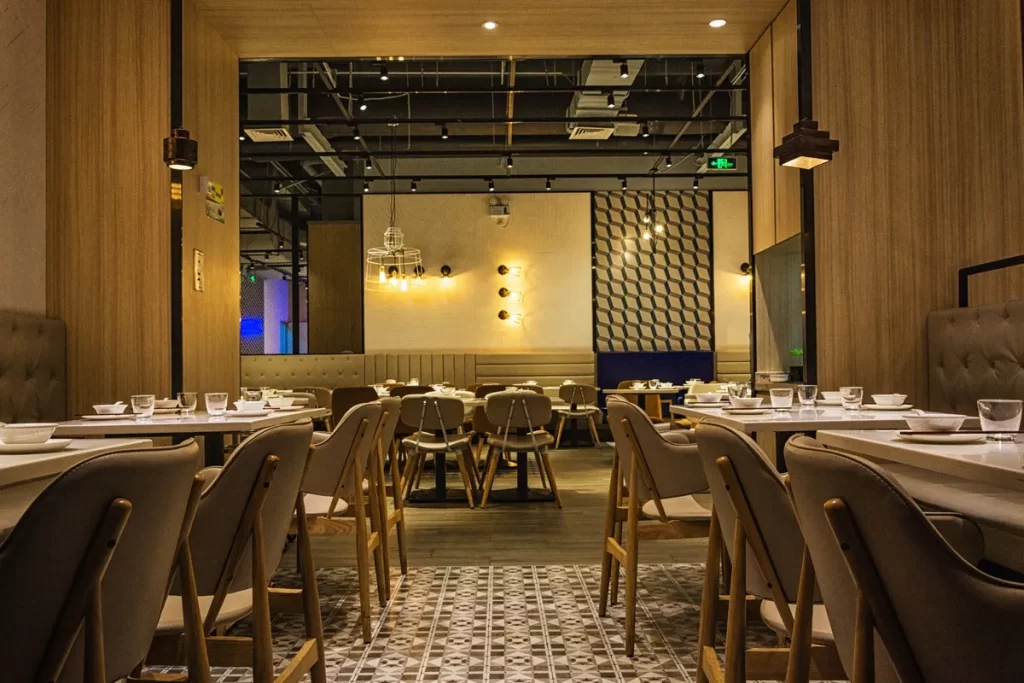 Interior de restaurante moderno e elegante com mesas de jantar preparadas, cadeiras de design contemporâneo, iluminação suave e piso decorado com padrões geométricos.