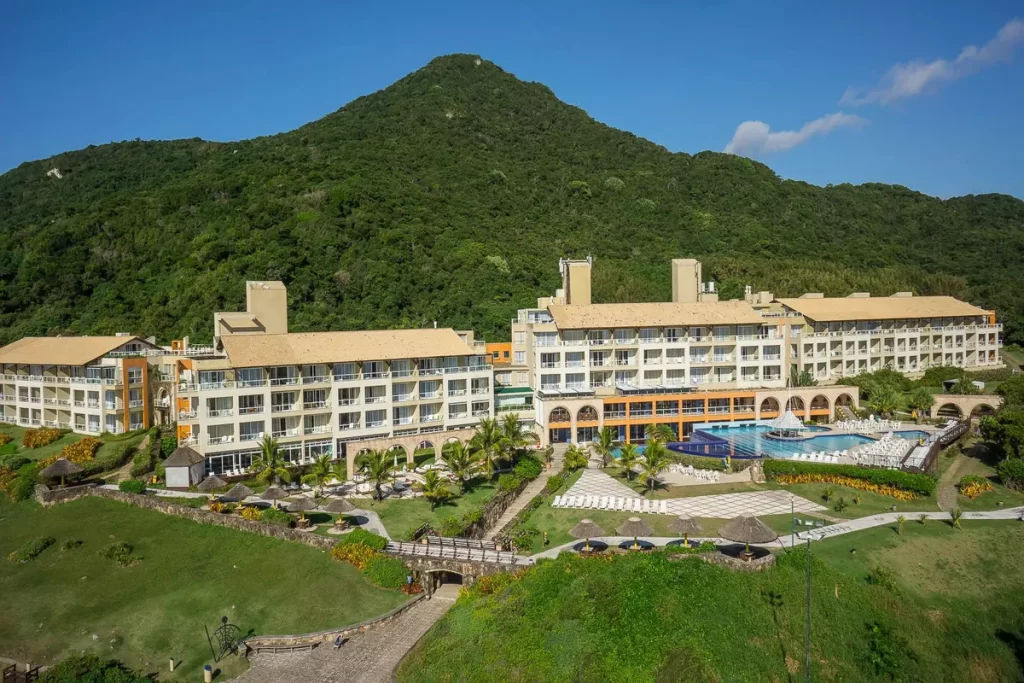 Resort de luxo cercado por natureza na base de uma montanha, com piscinas e áreas de lazer ao ar livre.
