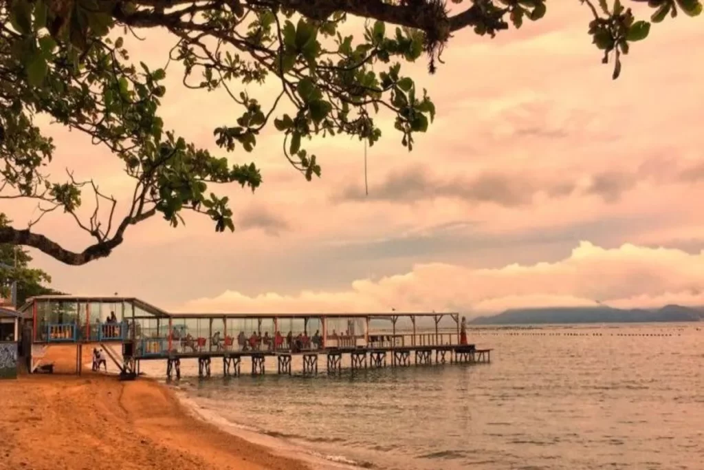 Píer do restaurante Ostradamus em Florianópolis com mesas sobre o mar ao pôr do sol