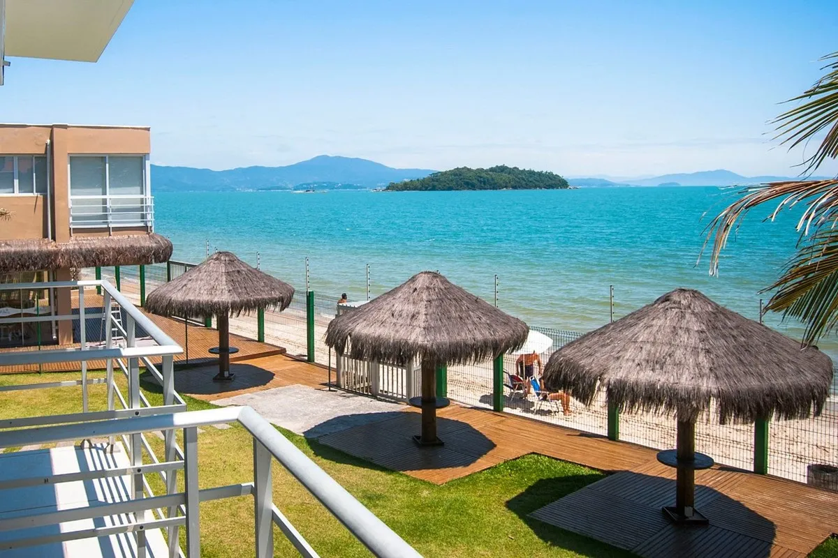 Varanda de quarto de frente para o mar com espreguiçadeira, guarda-sol e vista de ilha ao fundo.