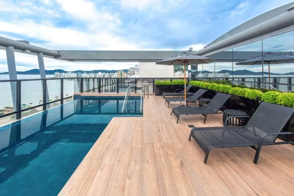 Piscina infinita em hotel de Florianópolis com vista panorâmica do mar e da cidade, espreguiçadeiras e guarda-sóis.
