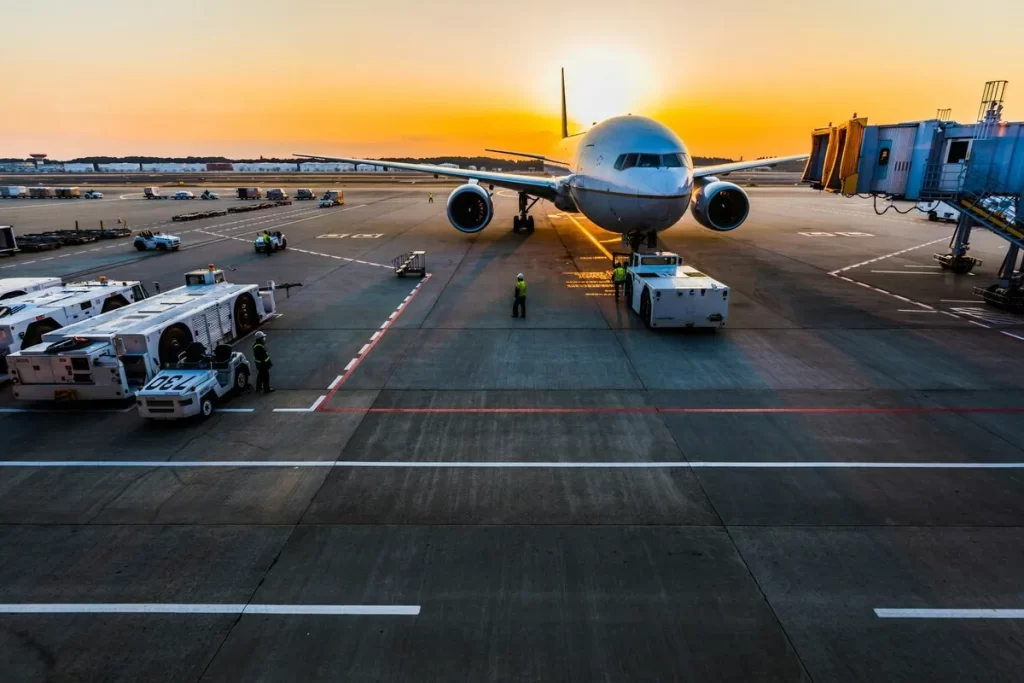 Avião no pátio do aeroporto ao pôr do sol, com equipamentos de solo e finger de embarque, simbolizando viagens aéreas e a proximidade de hotéis.