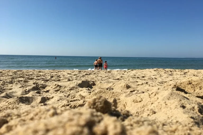 Praia de Jurerê Internacional com ondas na areia dourada, rochas costeiras e céu azul, em Florianópolis.