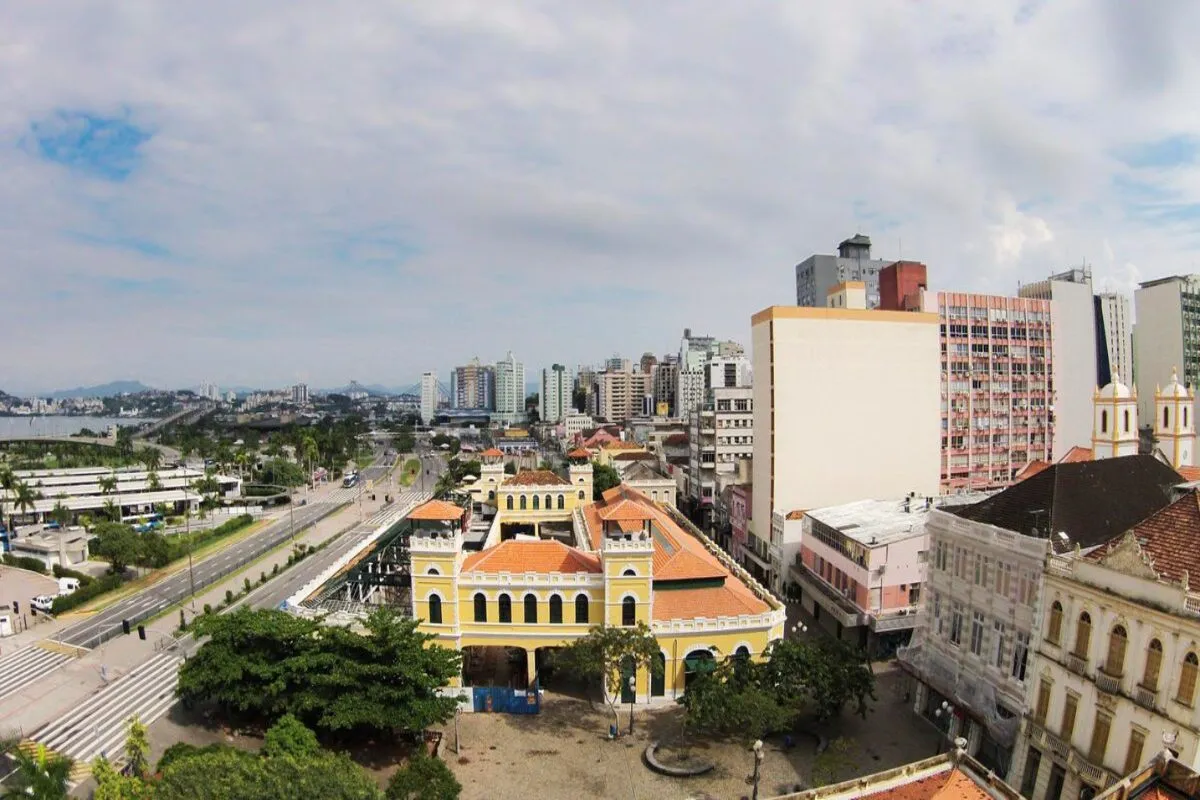 Edifício amarelo do Centro Histórico de Florianópolis com fonte e esculturas, pombos voando, céu azul.
