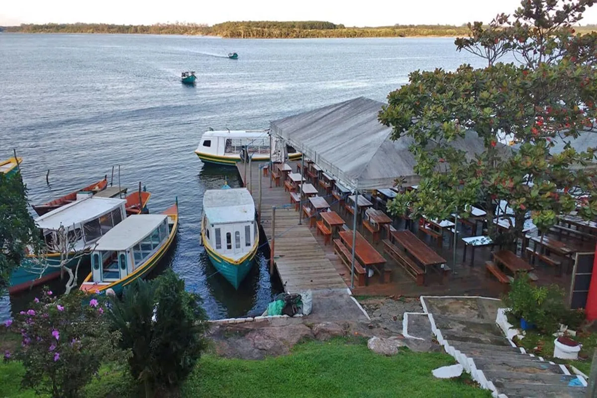 Restaurante à beira da água com mesas e barcos atracados, oferecendo vista para a Lagoa da Conceição em Costa da Lagoa, Florianópolis.