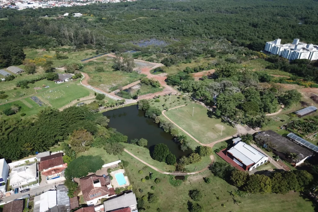 Visão panorâmica aérea do Jardim Botânico de Florianópolis, mostrando sua vasta área verde, lagos, trilhas, estufas e a integração com a área urbana e edificações ao redor.
