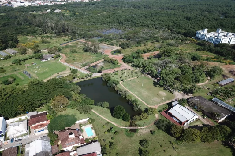Visão panorâmica aérea do Jardim Botânico de Florianópolis, mostrando sua vasta área verde, lagos, trilhas, estufas e a integração com a área urbana e edificações ao redor.