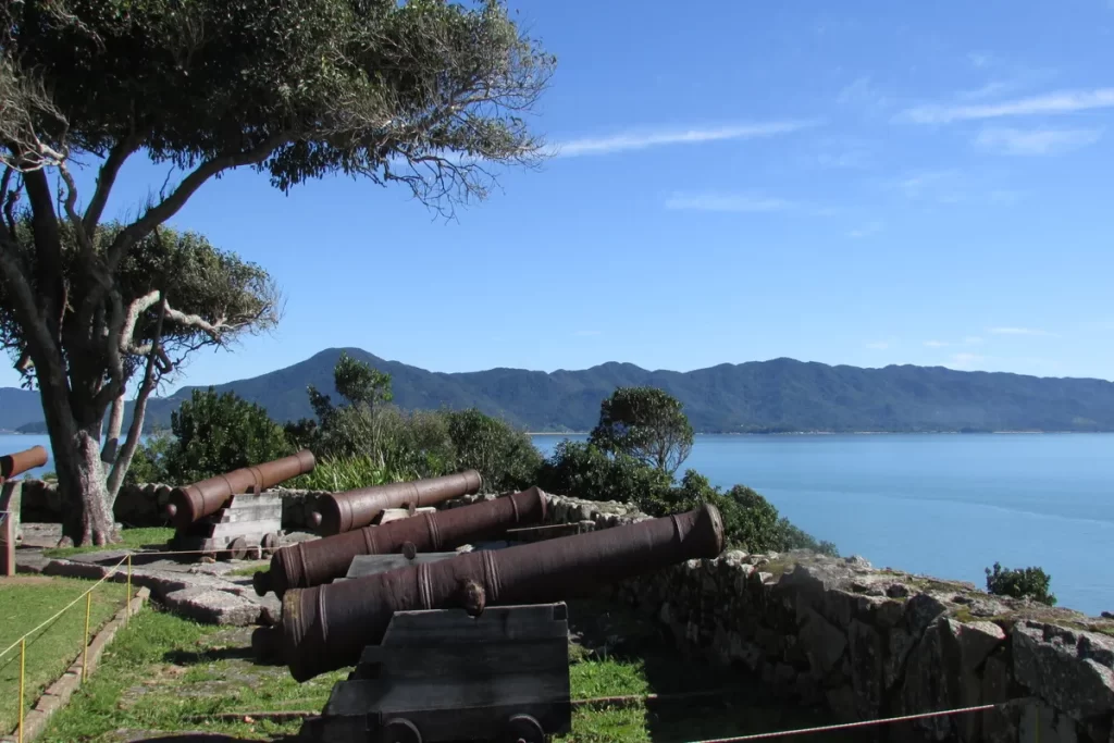 Canhões antigos no Forte de São João na Praia Forte em Florianópolis, com vista para o mar azul e montanhas ao fundo. Patrimônio histórico.