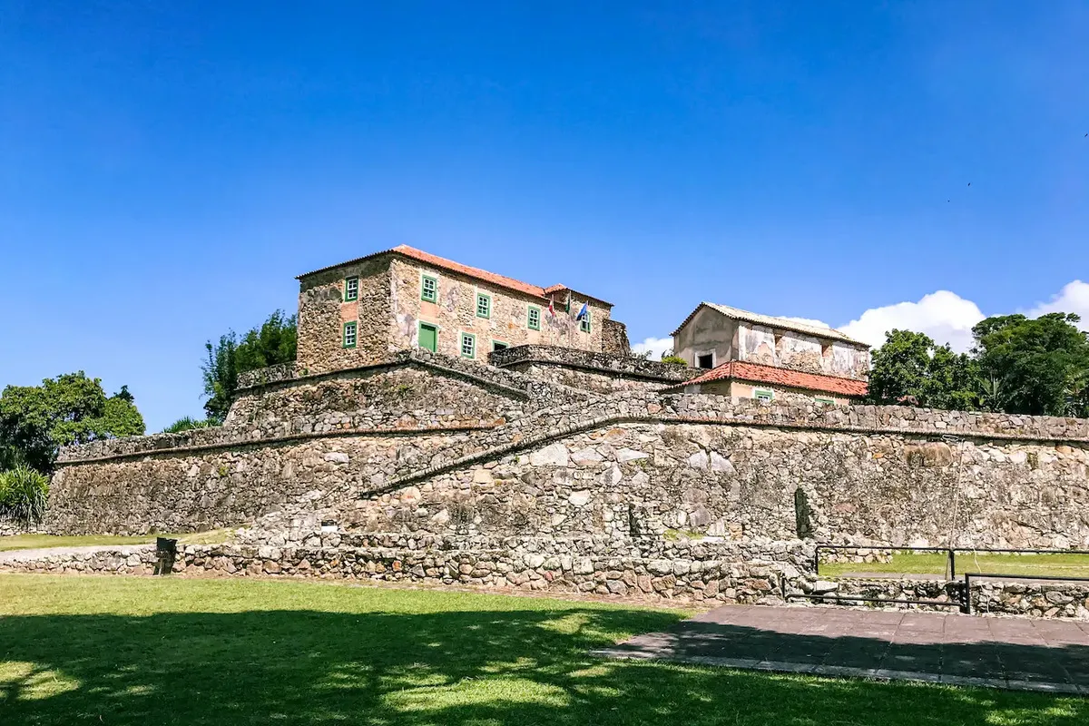 Forte de São José da Ponta Grossa na Praia Forte em Florianópolis, com suas muralhas de pedra e construções históricas sob céu azul.