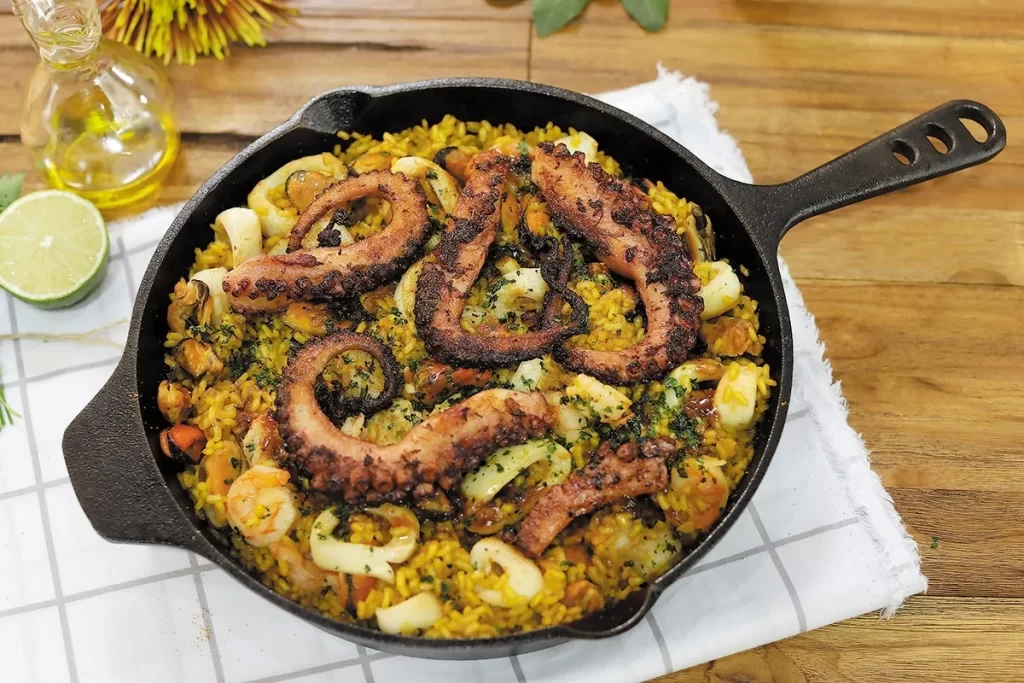Prato de paella ou arroz com frutos do mar em frigideira de ferro preta, contendo tentáculos de polvo grelhado, lula e mexilhões.