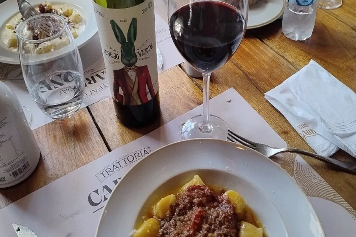 Mesa posta da Trattoria Carbone com prato de gnocchi com ragu, taça de vinho tinto e garrafa de vinho Coelho Verde.