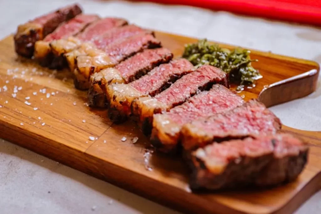 Cortes de picanha grelhada fatiada ao ponto, servidos em tábua de madeira com molho chimichurri e sal, prato de churrascarias em Florianópolis.