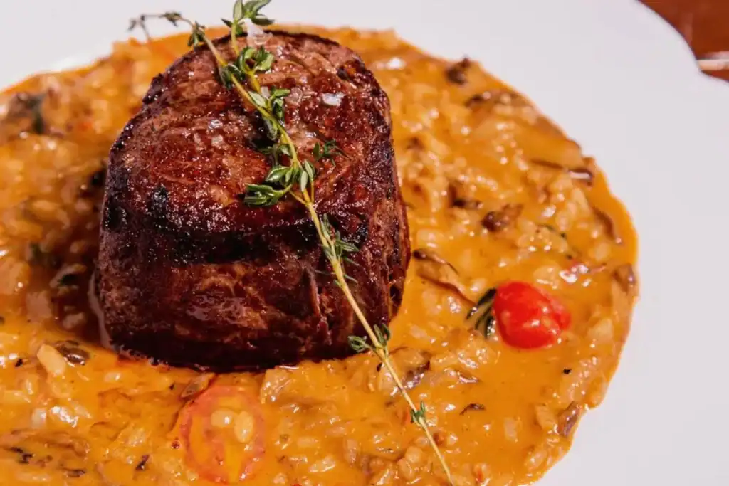 Filé mignon alto e suculento servido sobre risoto cremoso de tomate com ervas e tomate-cereja
