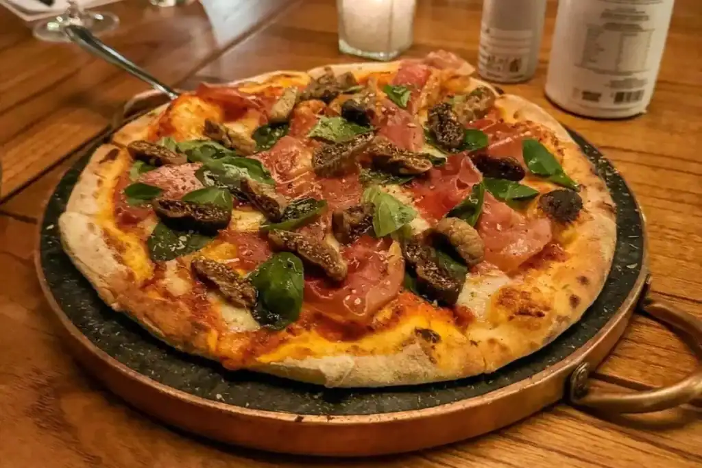 Pizza artesanal com presunto cru, figos assados e folhas de manjericão sobre massa crocante