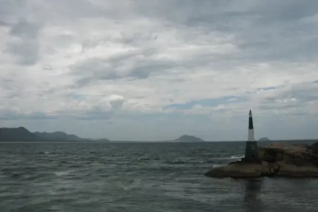 Farol da Barra da Lagoa em Florianópolis, localizado sobre rochas no mar com montanhas ao fundo