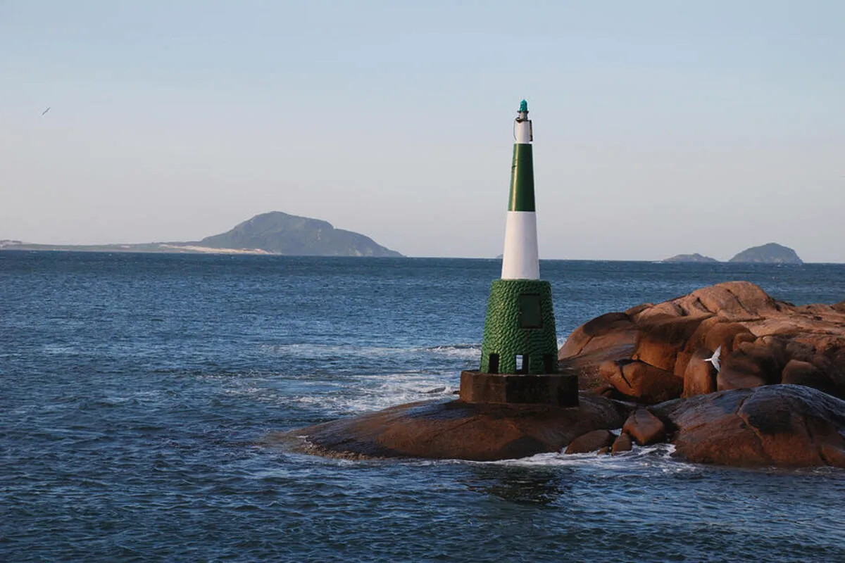 Farol da Barra da Lagoa em Florianópolis sobre pedras à beira-mar com oceano e ilhas ao fundo