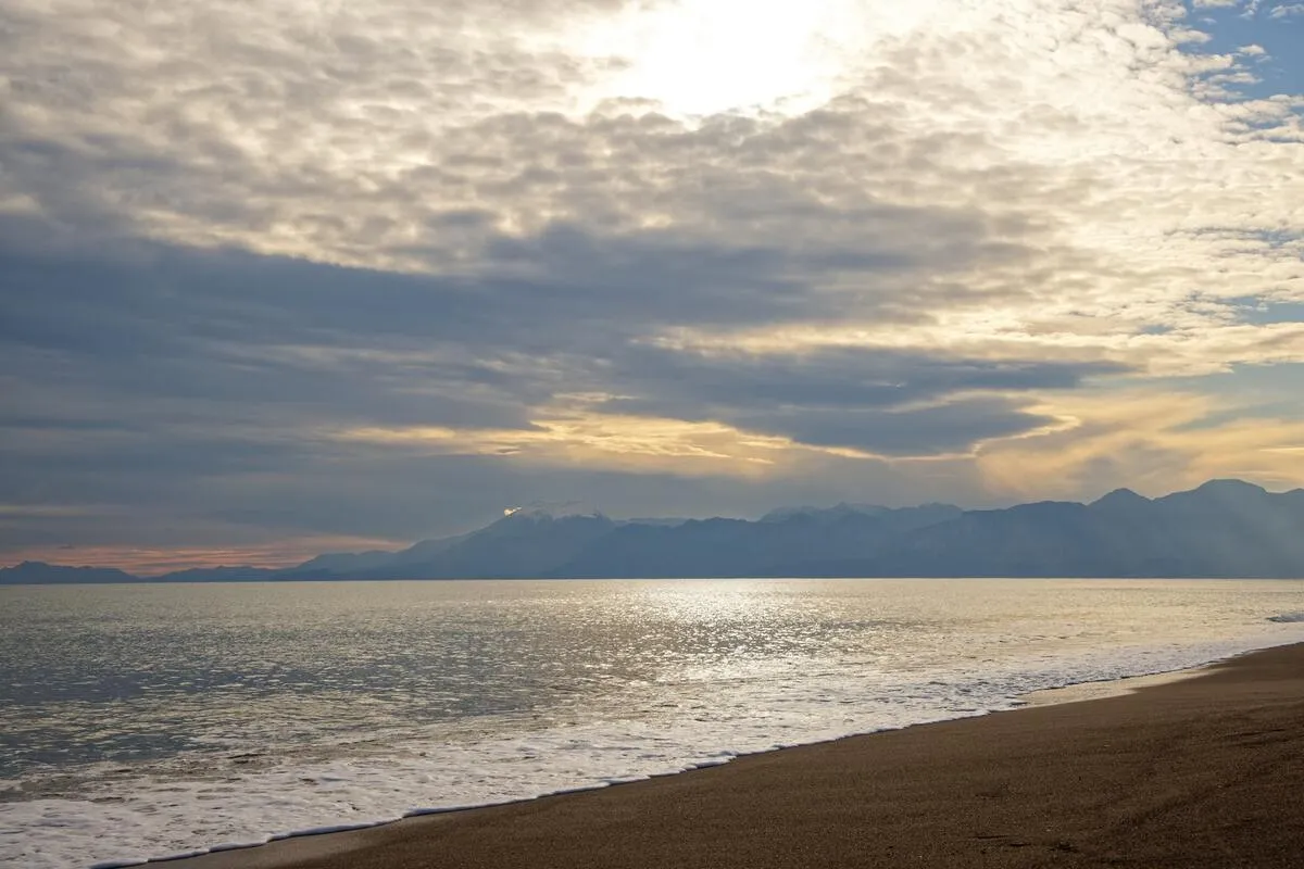 Vista de praia com mar calmo e nuvens carregadas refletindo a luz do sol, representando o fenômeno da maresia