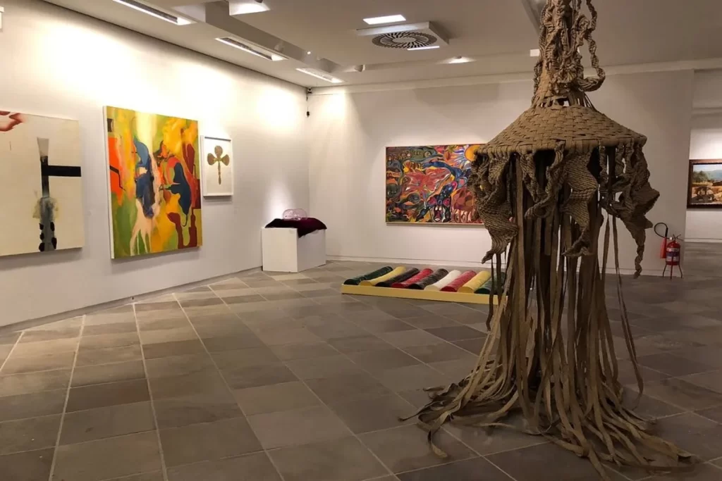 Exposição de arte contemporânea no Museu de Arte de Santa Catarina com esculturas, instalações e pinturas abstratas em ambiente moderno e iluminado.