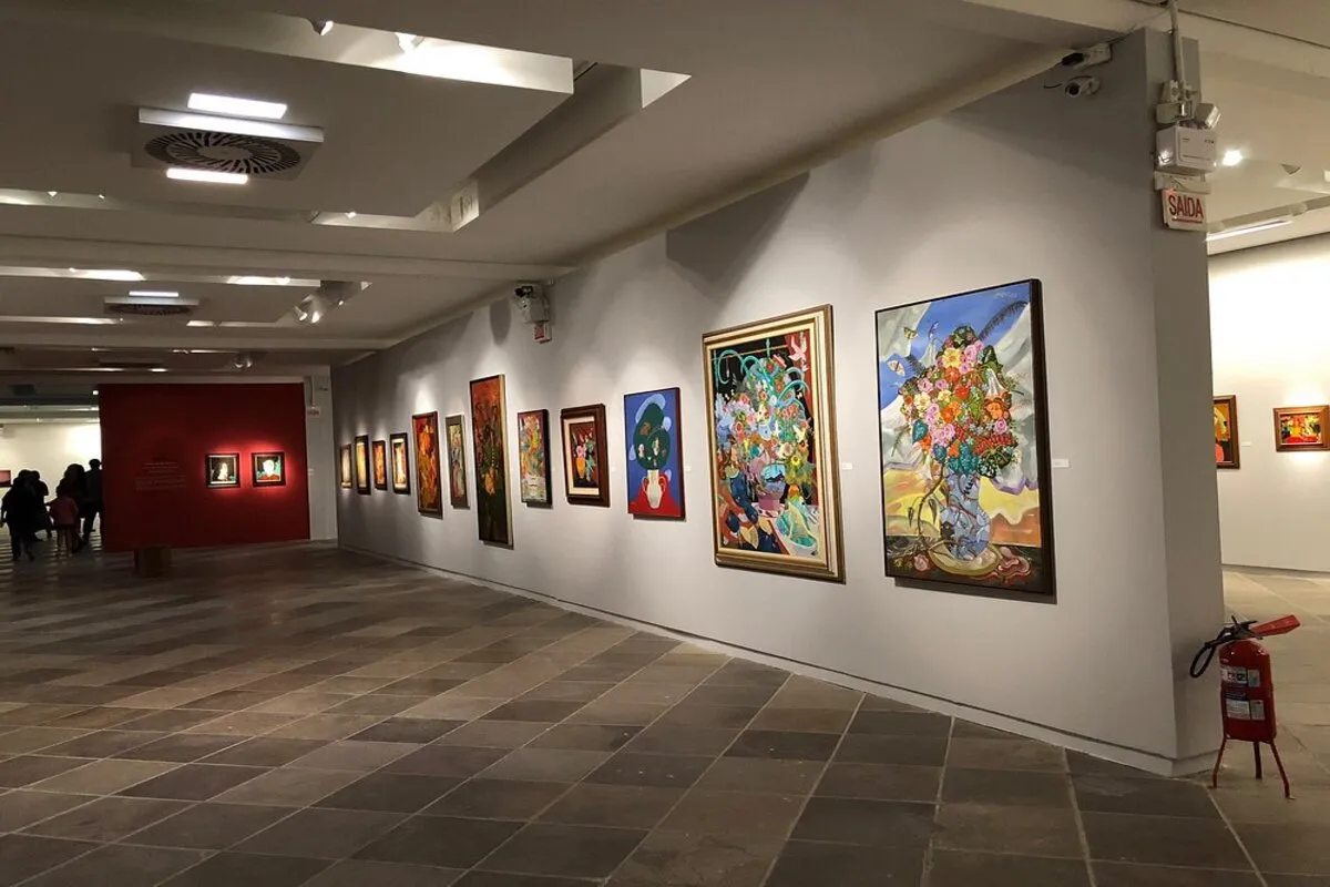 Exposição de pinturas coloridas no Museu de Arte de Santa Catarina em Florianópolis, com obras vibrantes emolduradas em destaque nas paredes da galeria.
