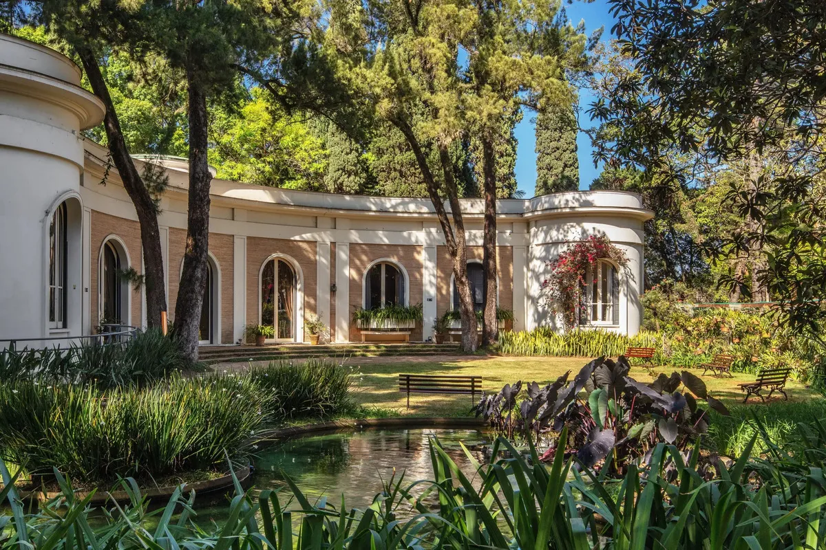 Jardim externo do Museu da Imagem e do Som de Santa Catarina (MIS-SC), em Florianópolis, com lago, árvores e bancos para descanso.