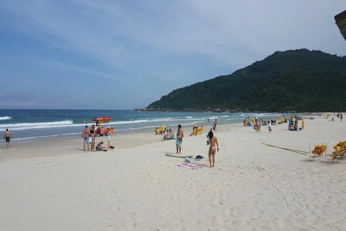 Praia Brava em Florianópolis com areia branca, mar azul e banhistas aproveitando o dia de sol.
