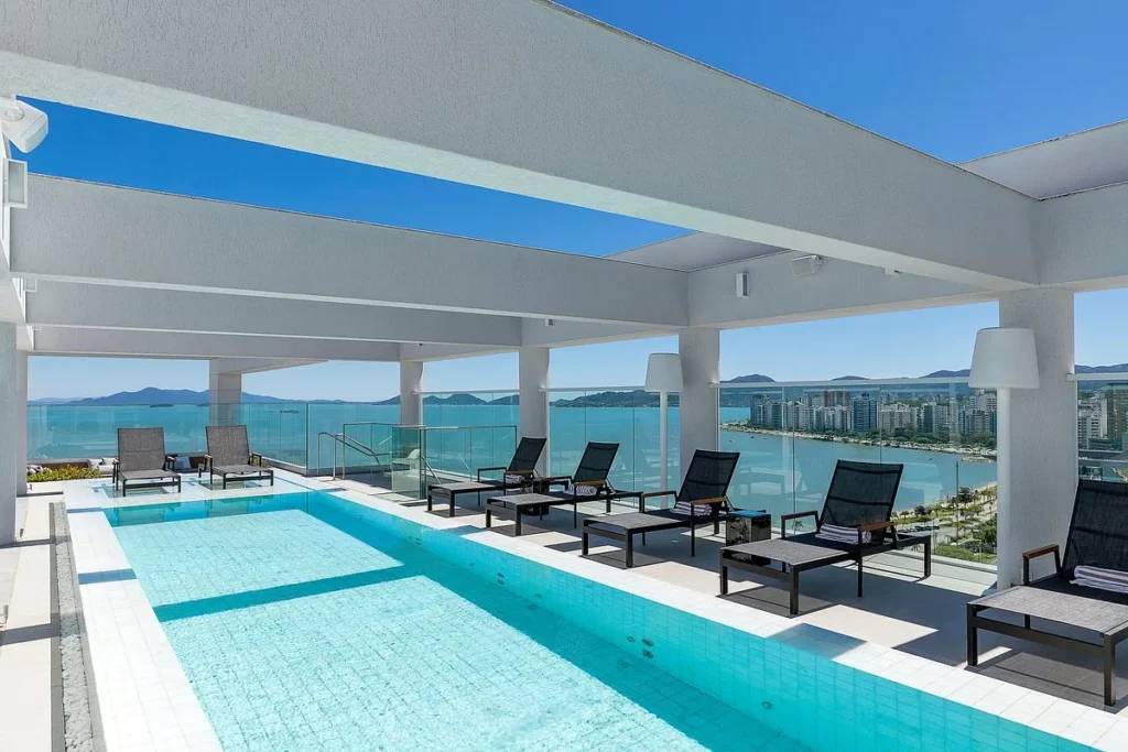 Piscina de hotel na cobertura com espreguiçadeiras e vista para o mar e cidade litorânea