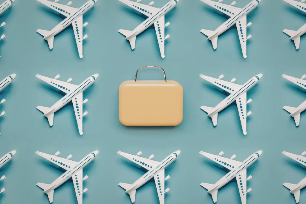 Miniaturas de aviões distribuídas sobre fundo azul com uma mala pequena no centro.