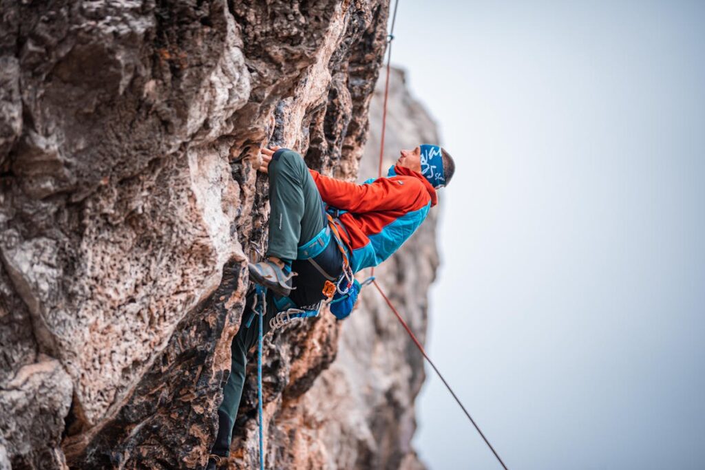Pessoa praticando escalada em rocha, presa por cordas de segurança em parede íngreme.