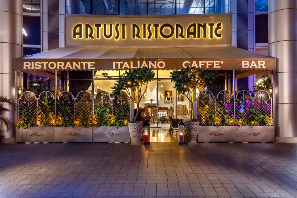 Fachada do Artusi Ristorante, restaurante italiano com iluminação noturna, mesas externas e decoração sofisticada