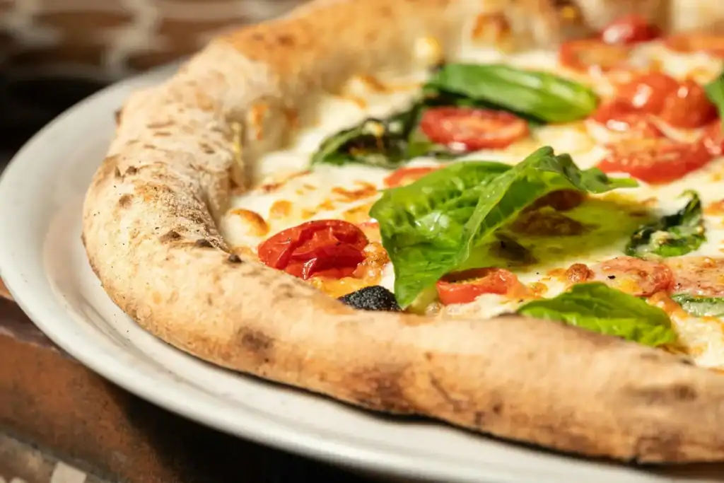 pizza artesanal com borda alta, queijo derretido, tomates e folhas de manjericão fresco