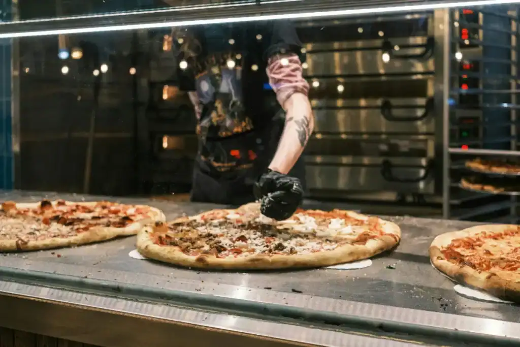 Pizzarias em Florianópolis. Pizzaiolo preparando pizzas em bancada com várias massas abertas dentro de cozinha profissional
