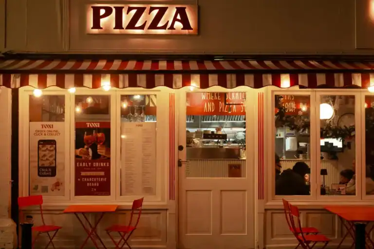 fachada de pizzaria iluminada à noite com mesas externas e letreiro escrito pizza