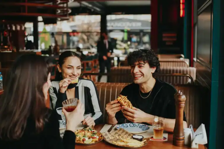 grupo de amigos sorrindo enquanto comem hambúrguer e petiscos em restaurante casual
