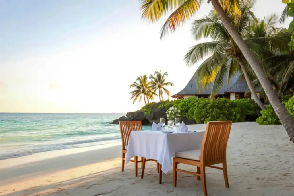 mesa de jantar na areia próxima ao mar com coqueiros e paisagem tropical ao redor