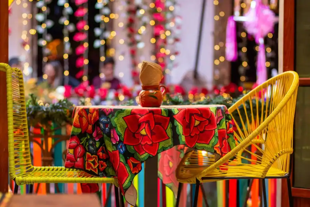Restaurantes mexicanos em Florianópolis. Mesa com toalha colorida e cadeiras em ambiente decorado com luzes e elementos mexicanos
