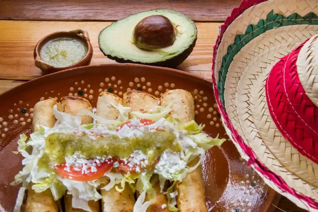 Prato com burritos cobertos com molho, acompanhados de guacamole e abacate