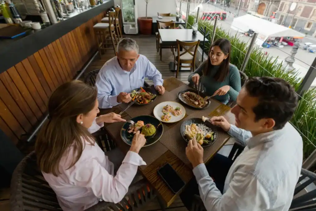 Restaurantes para família Florianópolis. Grupo de pessoas almoçando em restaurante com varanda e vista externa enquanto compartilham pratos