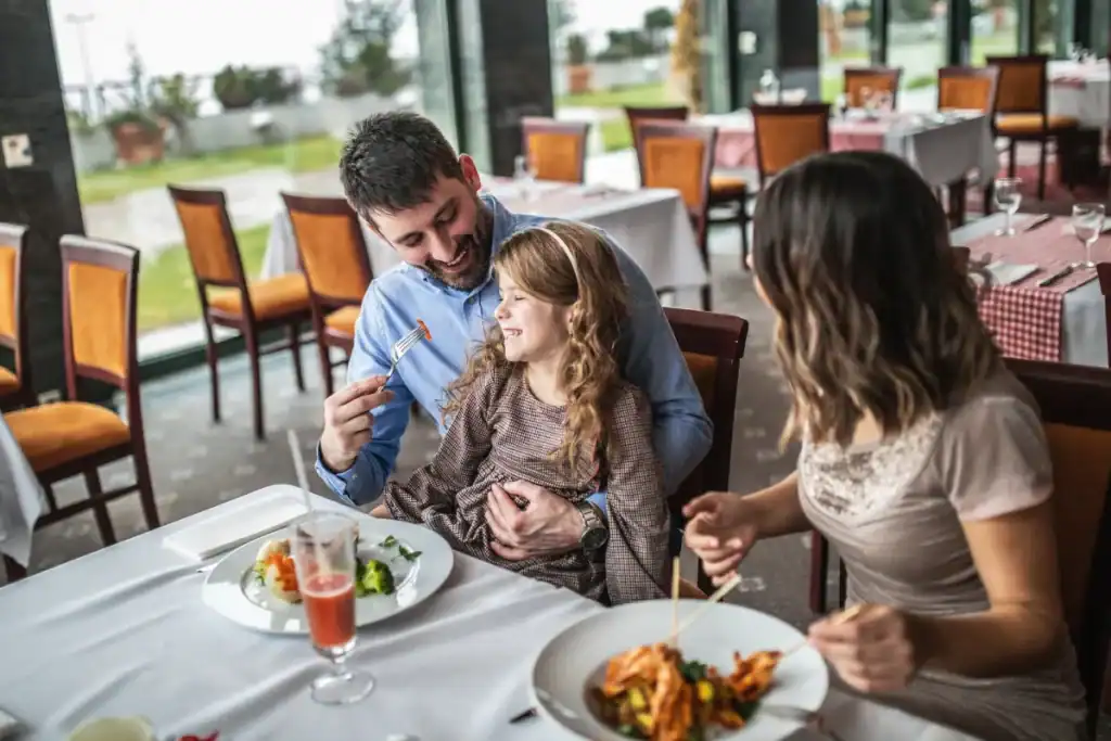 família com criança pequena sorrindo enquanto come em restaurante com mesas organizadas e ambiente iluminado