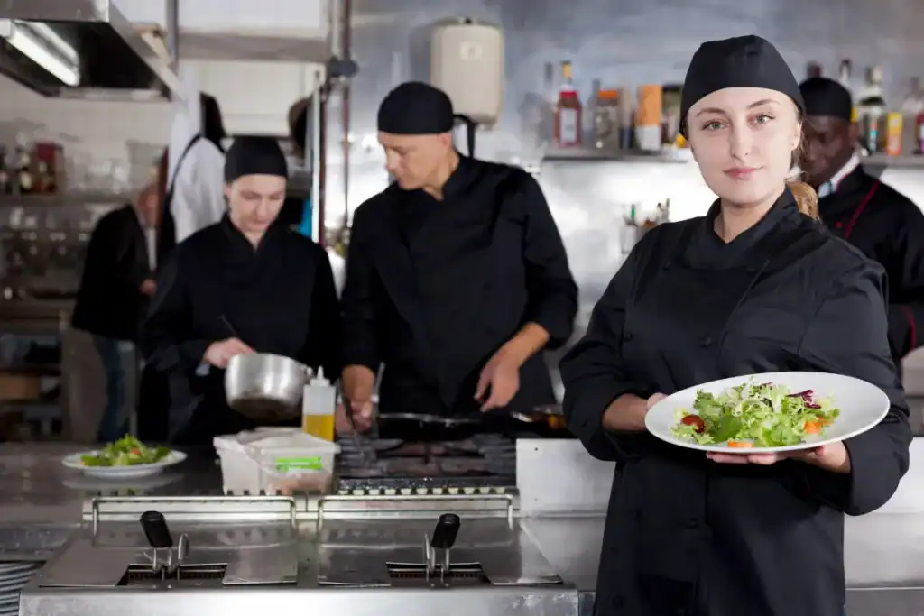 Restaurantes saudáveis Florianópolis. Equipe de cozinha preparando alimentos enquanto uma chef segura um prato de salada