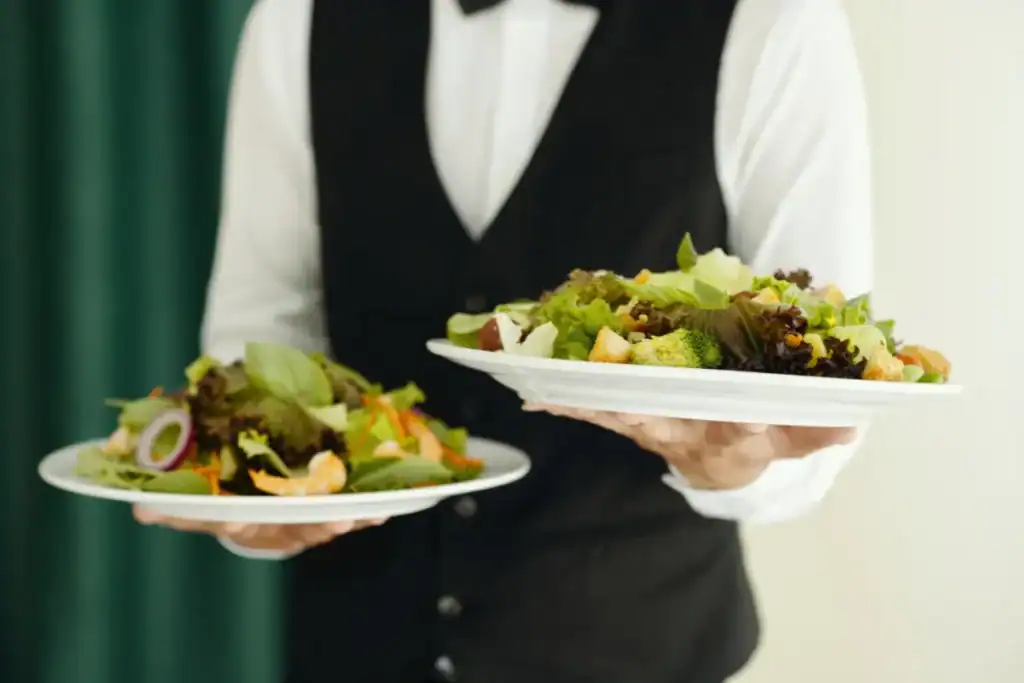 garçom segurando dois pratos de salada com folhas verdes e legumes variados