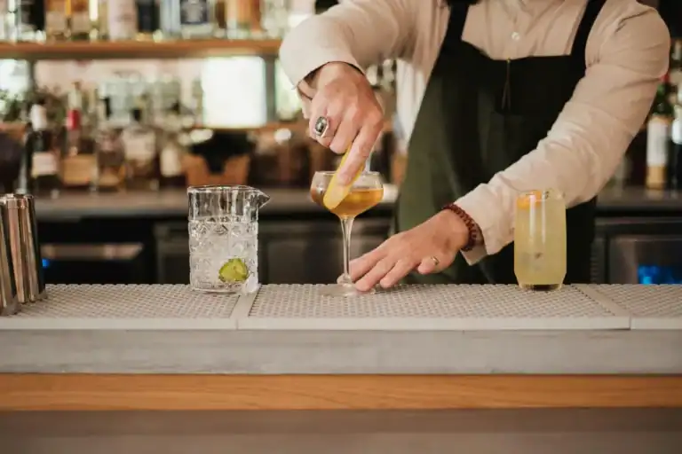 bartender finalizando um coquetel com casca de laranja sobre o balcão de um bar