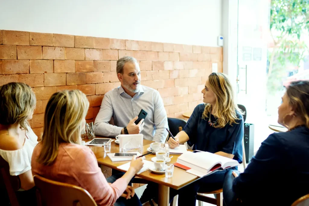 Cafés em Florianópolis. Grupo de pessoas reunidas em mesa de cafeteria com xícaras de café, cadernos e celular durante uma conversa