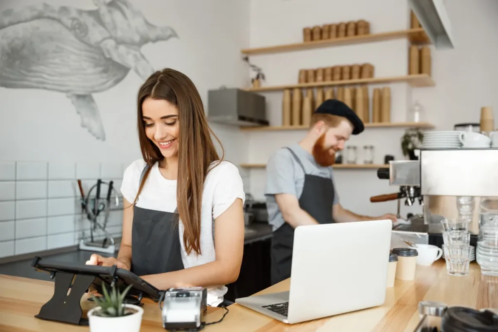 cafeterias na Lagoa da Conceição. Funcionária de cafeteria utilizando sistema de caixa enquanto barista prepara café ao fundo em ambiente moderno