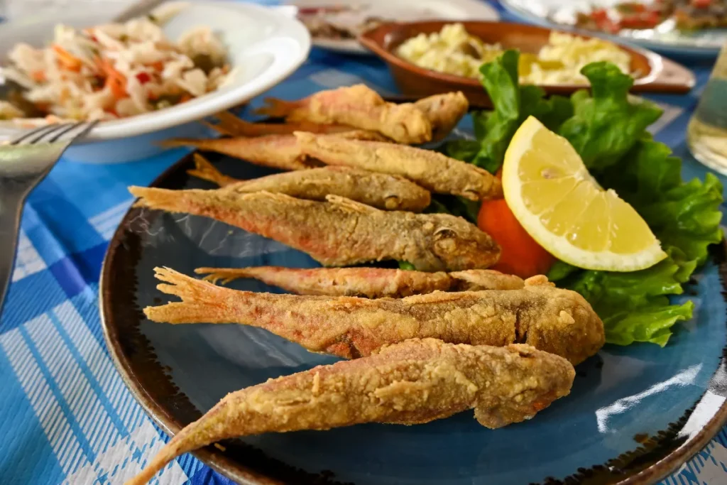 Prato com peixes fritos inteiros acompanhados de limão, salada e outros pratos ao fundo em Florianópolis