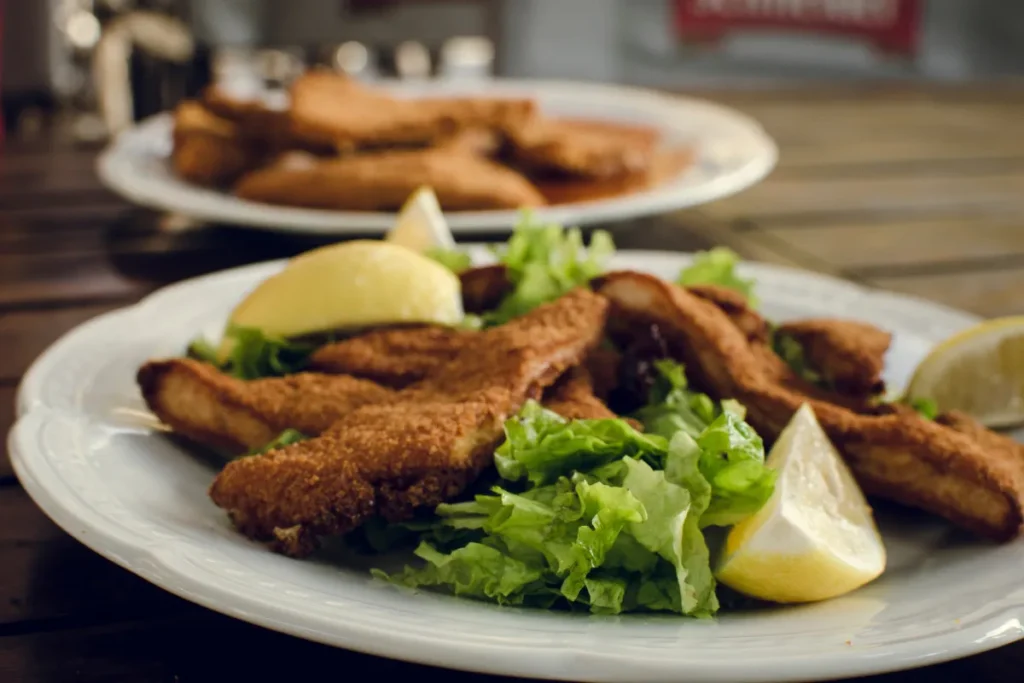 Prato com filé de peixe frito servido com alface e limão em mesa de restaurante