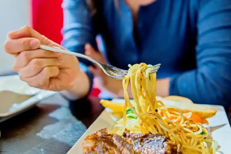 Pessoa enrolando espaguete no garfo enquanto almoça um prato com carne e massa em restaurante