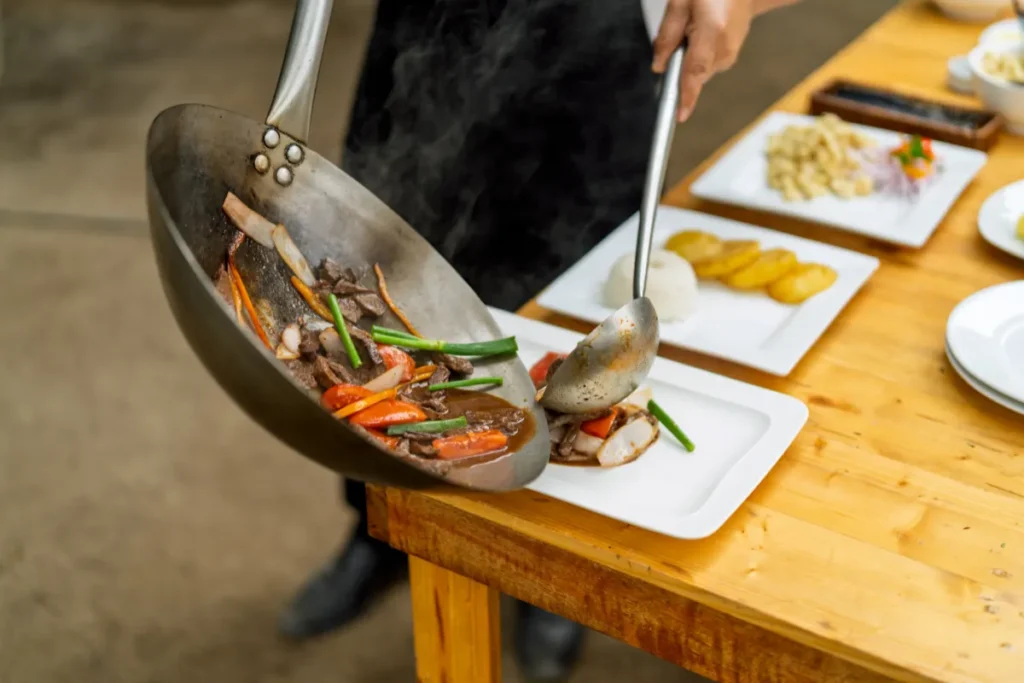 Cozinheiro servindo prato quente com legumes e carne em cozinha profissional