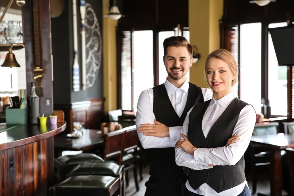 dois atendentes de restaurante sorrindo com braços cruzados em frente ao balcão em ambiente interno