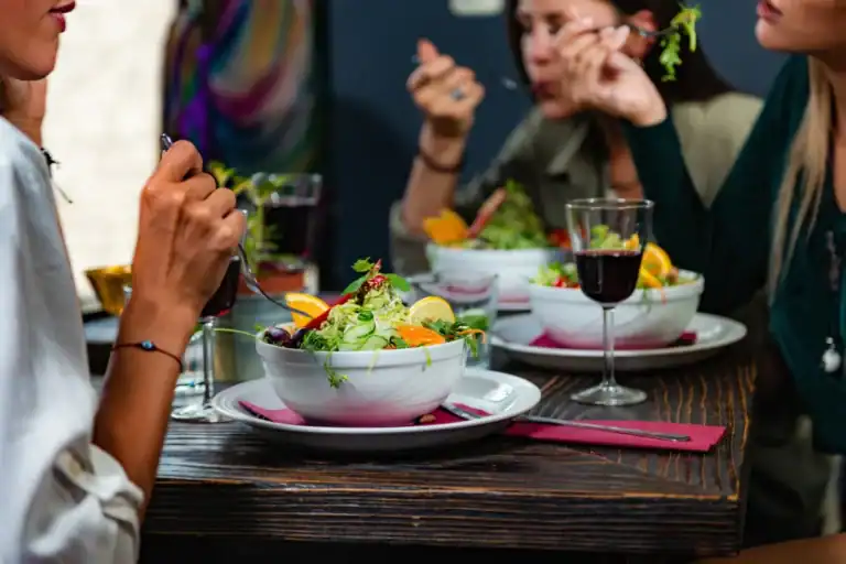 grupo de pessoas sentado à mesa em restaurante com pratos de salada e taças de vinho durante uma refeição