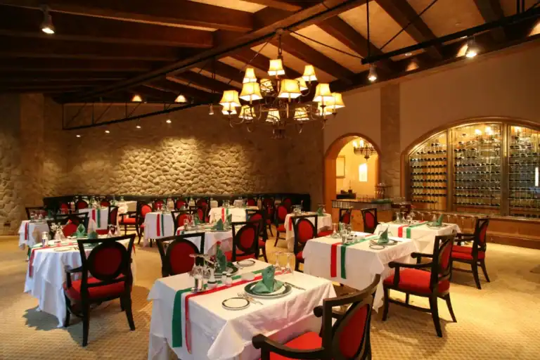 salão interno de restaurante com decoração rústica, mesas organizadas com toalhas e cadeiras vermelhas iluminadas por lustre